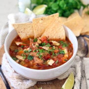 Closeup of a white bowl with pulled pork tortilla soup and ingredients behind it.