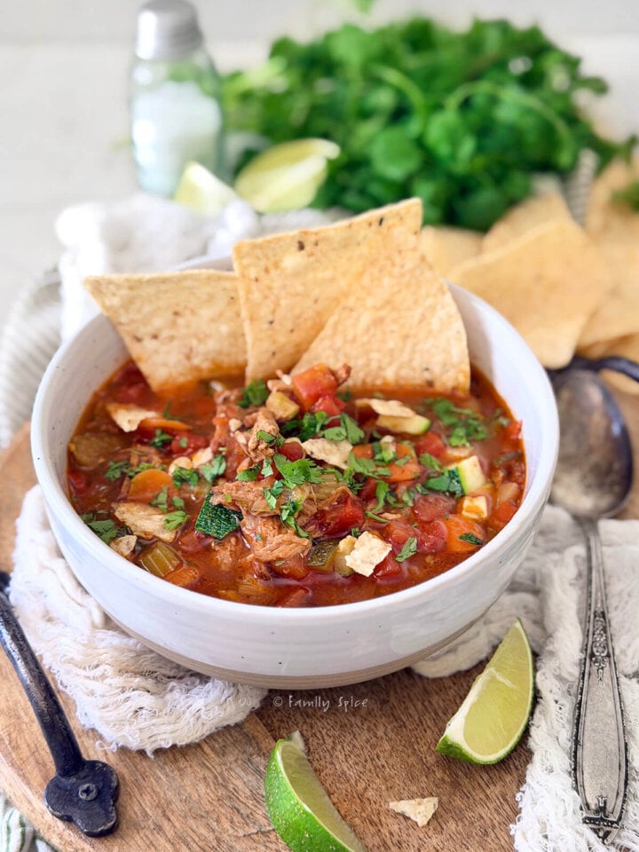 Closeup of a white bowl with pulled pork tortilla soup and ingredients behind it.