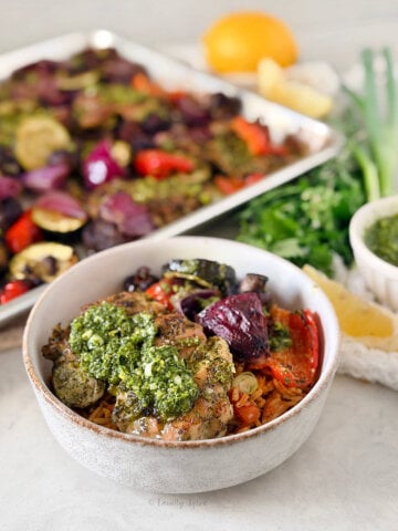 Closeup of a bowl with chicken chimichurri with vegetables in it with the remaining on a sheet pan behind it.